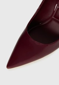 Chaussure à talon aiguille bourgogne à bout pointu avec une finition lisse et brillante, et doublure intérieure détaillée visible.