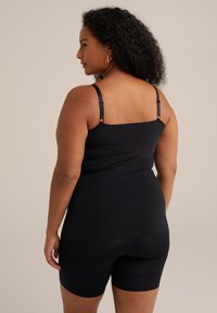 Črn top brez rokavov z nastavljivimi naramnicami v kombinaciji s črnimi oprijetimi kratkimi hlačami, ki prikazujejo gladko teksturo in oblikovalen dizajn.