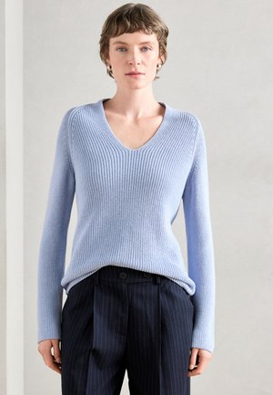 Pull en maille bleu clair avec un col en V, manches longues, tissu texturé et coupe décontractée, associé à un pantalon foncé à rayures.