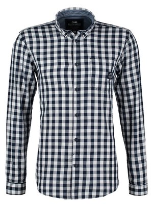 Mand går og bærer en sort og hvid ternet skjorte, grå jeans, sneakers og en sort crossbody taske med brun rem.