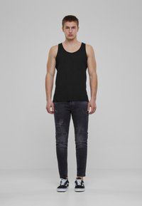 Top sin mangas de algodón negro con tirantes anchos, combinado con jeans ajustados de mezclilla oscura y desgastada. El modelo lleva zapatillas en blanco y negro.