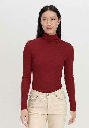 Rode longsleeve coltrui gemaakt van zacht materiaal, getailleerd ontwerp met een hoge kraag. Gecombineerd met lichte beige high-waisted jeans.