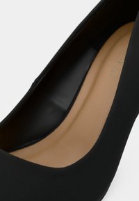 Gros plan d'une chaussure à talon noir montrant l'extérieur lisse et la semelle intérieure rembourrée beige.