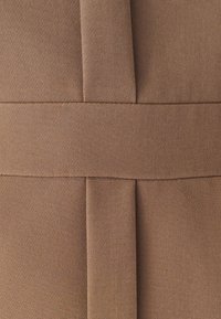 Hnědá látka s texturovanou tkaninou, včetně plochého švu a záhybů pro přidanou dimenzi. Design je elegantní a strukturovaný.
