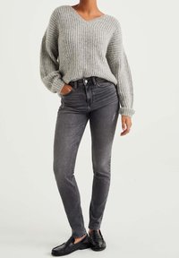 Šedý žebrovaný pletený svetr s výstřihem do V, kombinovaný s černými skinny džíny s vysokým pasem a černými mokasíny. Měkká textura a volný střih.