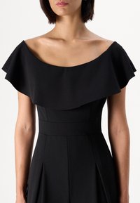 Melnā kleita ar bezplecu dizainu, ruffles izgriezumu, pieguļošu augšdaļu un plisētu svārku. Gluda tekstūra un tīras līnijas.