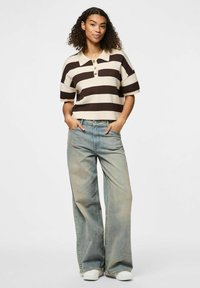 Polo shirt cintré avec des rayures beiges et brunes, doté d'un col et de trois boutons. Jeans larges délavés, chaussures blanches, look décontracté.