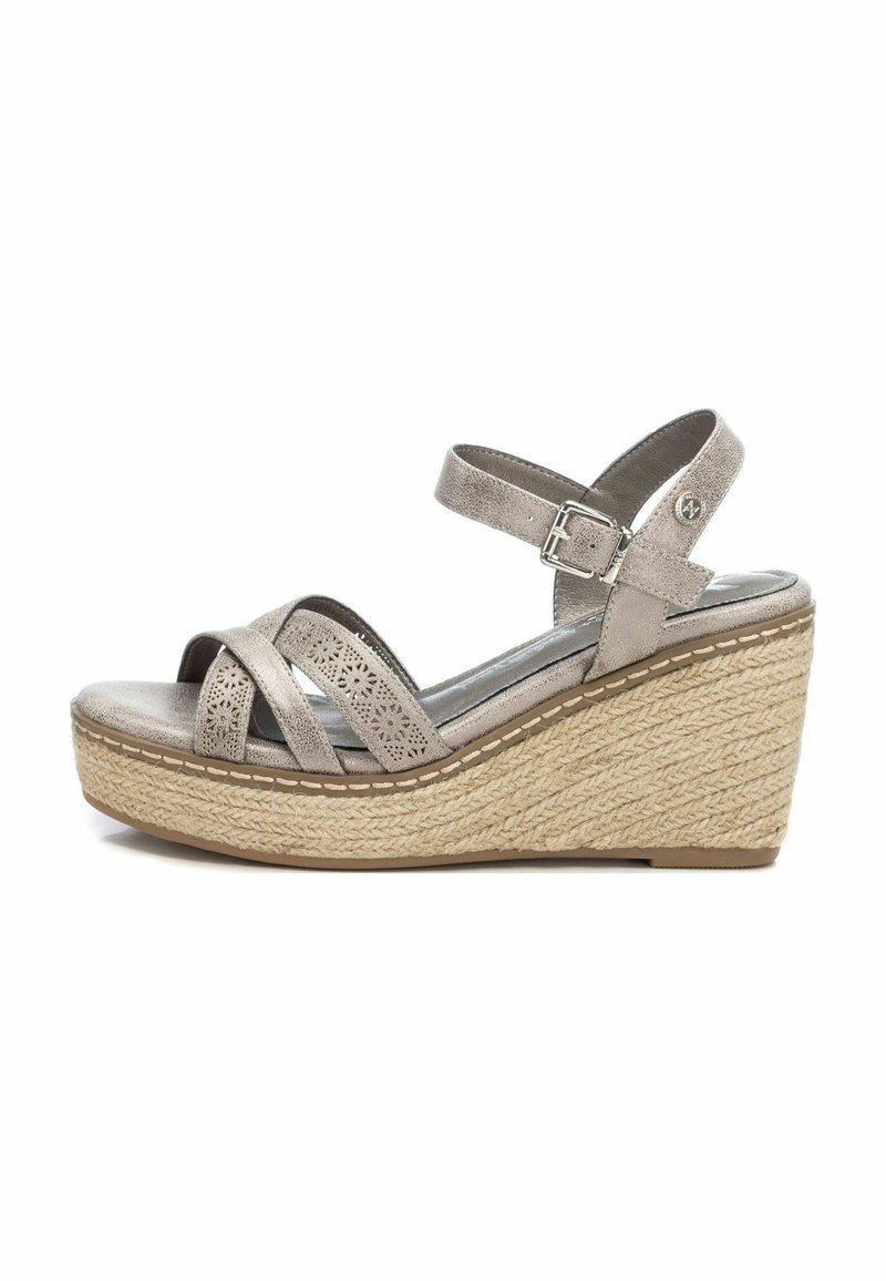 Sandal gris de cuña con tiras cruzadas, hecho de material suave. Presenta intrincados diseños recortados y una suela de yute trenzado. Cierre de hebilla en el tobillo.