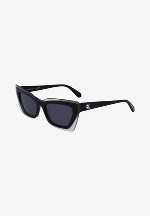 Black oversized sunglasses with a geometric shape, featuring dark lenses and a contrasting grey detail on the frame. Logo on the arm.