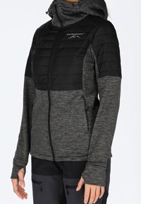 Szara i czarna kurtka zapinana na zamek z pikowaną górną częścią, kapturem i mankietami z otworami na kciuki. Miękka w dotyku; na piersi znajduje się logo.