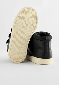Baskets montantes noires avec une tige en cuir lisse et une semelle en caoutchouc texturé. Fermeture avec sangle auto-agrippante et col rembourré pour plus de confort.