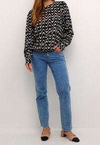 Czarno-biała bluzka z długim rękawem w falowany wzór, zestawiona z jasnoniebieskimi spodniami z prostymi nogawkami i dwukolorowymi butami na słupku.