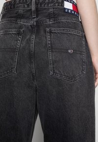 Černé džíny z denimu se vybledlým vzhledem, se dvěma zadními kapsami a malou nášivkou v červené, bílé a modré barvě na pasu.