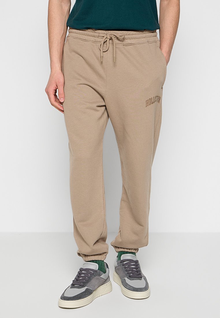 Beżowe spodnie dresowe z elastycznym pasem i regulowanym sznurkiem, z małym logo "Hollister" z przodu. Fakturowana tkanina.