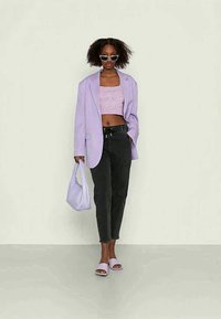 Lilac oversized blazer over a pink cropped top, black tapered jeans, lilac handbag, and matching slide sandals. Accessories include sunglasses.