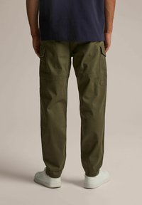 Zielone spodnie cargo z wieloma kieszeniami, luźnym krojem i gładką fakturą, w połączeniu z białymi trampkami. Widok z tyłu.