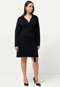 Vestido negro de manga larga con escote en V y cuello, que presenta un cinturón atado en la cintura, hecho de una tela de punto texturizada.
