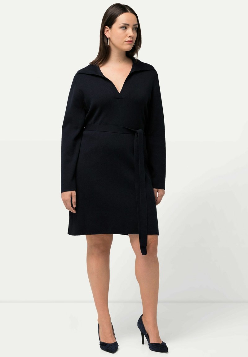 Vestido negro de manga larga con escote en V y cuello, que presenta un cinturón atado en la cintura, hecho de una tela de punto texturizada.
