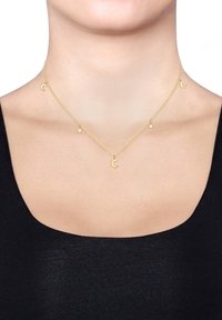 Kuldvärviline kihiline kaelakee, millel on väikesed kuu ja tähe talismanid õrna kettiga. Sile tekstuur ja minimalistlik disain.