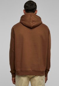 Felpa con cappuccio marrone realizzata in materiale morbido. Presenta una vestibilità comoda con tasca a marsupio e polsini e orlo a costine.