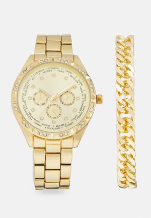Gold-tone watch with link band, features a textured bezel, round face, multiple time zones, and crystal accents. Includes a matching chain bracelet.