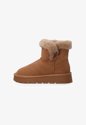 Brązowy zamszowy botek za kostkę z grubą gumową podeszwą, futrzanym mankietem i zapięciem na toggle po bokach na białym tle.