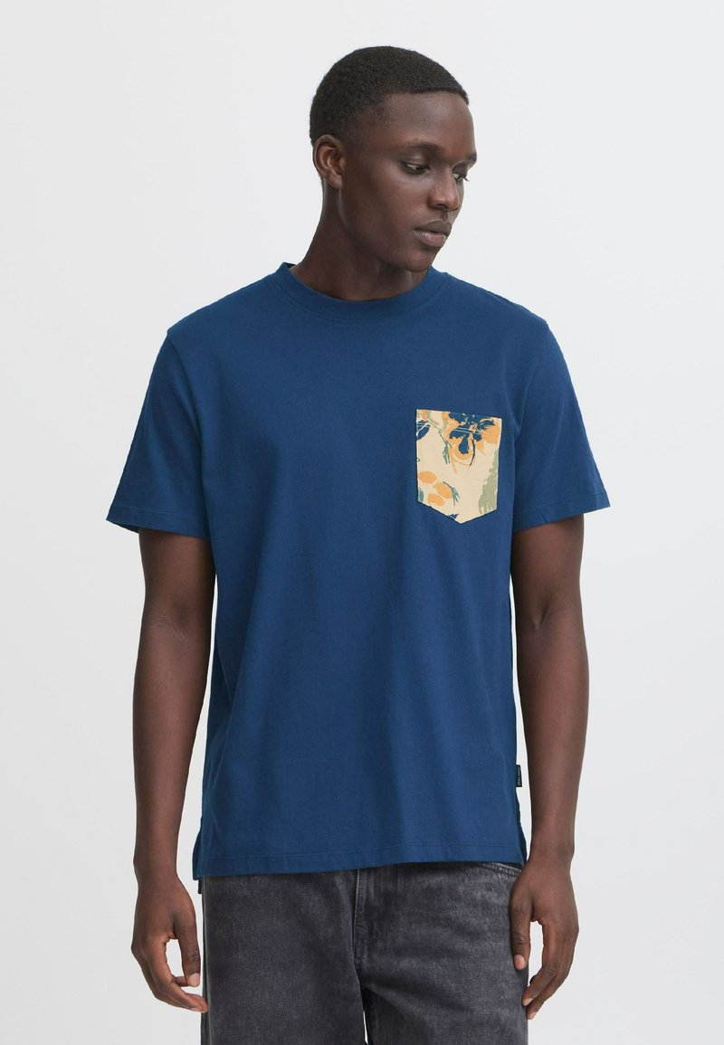 Mørkeblå bomulds t-shirt med korte ærmer og en mønstret cremet lomme med blomsterdesign i blå og orange. Enkel, afslappet pasform.