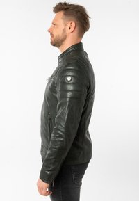 Dunkelgrüne Lederjacke mit strukturiertem Schnitt, gerippten Schulterakzenten und Reißverschluss. Verfügt über Seitentaschen und ein kleines Logopatch.