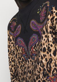 Sweatshirt i svart tyg med färgglada paisleymönster och leopardtryck på den nedre halvan. Textur och djärva mönster genom hela plagget.