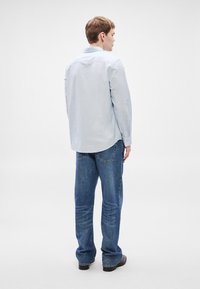 Gaiši zila krekla blūze ar garām piedurknēm, kombinēta ar vaļīgām zilām džinsām. Krekla apakša ir apaļa, ar parastu apkakli.