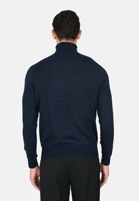 Maglione a collo alto di colore blu navy realizzato in un tessuto leggero a maglia, caratterizzato da maniche lunghe, polsini e orlo a coste, cuciture visibili e una vestibilità aderente.