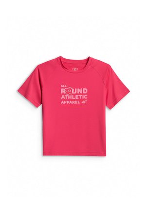 Młoda dziewczyna stoi, ubrana w różowy sportowy t-shirt z krótkim rękawem, czarne spodenki, białe skarpetki i czarne tenisówki na jednolitym szarym tle.