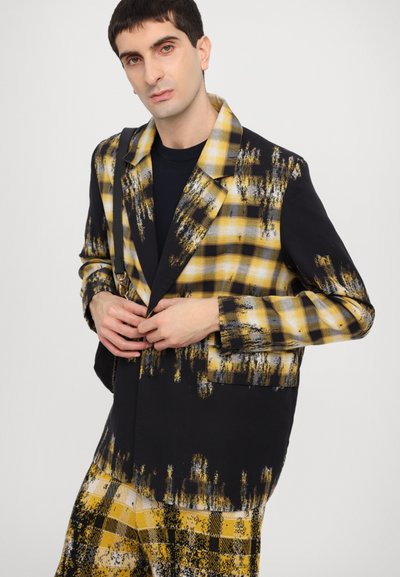 Black and yellow plaid blazer with a brushed texture, featuring a relaxed fit, notched lapels, and visible stitching details.