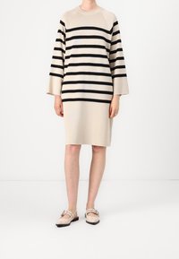 Abito beige con strisce orizzontali nere, maniche a lunghezza gomito e una vestibilità comoda. Abbinato a scarpe basse di colore chiaro.