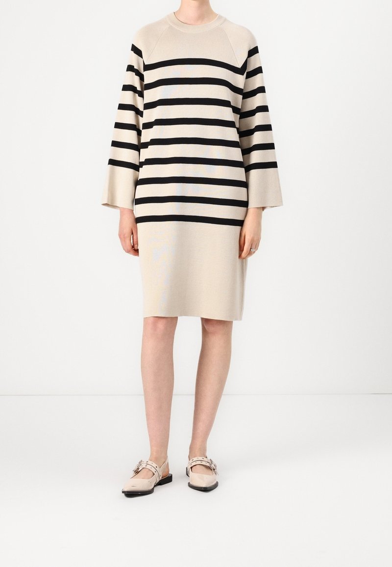Abito beige con strisce orizzontali nere, maniche a lunghezza gomito e una vestibilità comoda. Abbinato a scarpe basse di colore chiaro.