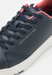 Sneaker in pelle blu navy con lacci rosa, suola bianca e logo dorato. Lati texturizzati con cuciture decorative e accento multicolore sul tallone.