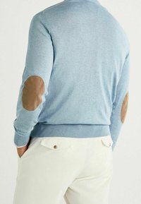 Jasnoniebieski sweter z dzianiny, z brązowymi łatami na łokciach, ściągaczami na mankietach i pasie. Prosty krój, bez kołnierza, widok od tyłu.