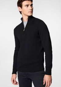 Czarny sweter dzianinowy z kołnierzem na ćwierć zamek, długimi rękawami i ściągaczami, noszony na szarym T-shircie. Gładka tekstura i dopasowany fason.