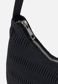 Sort tekstureret stof håndtaske med rynket design, udstyret med en sølv lynlås og en smal, flad rem.