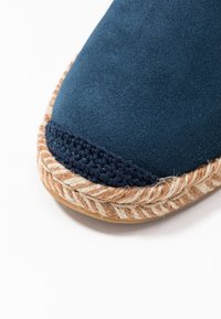 Espadrille de ante azul marino con suela de yute trenzado. Presenta un acento de ganchillo en la punta, que resalta su detalle texturizado.