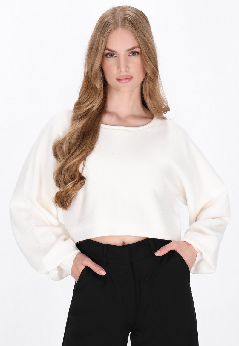 Pull court en tissu doux et blanc avec un col rond et des manches larges, associé à un pantalon noir taille haute. Texture lisse, design simple.