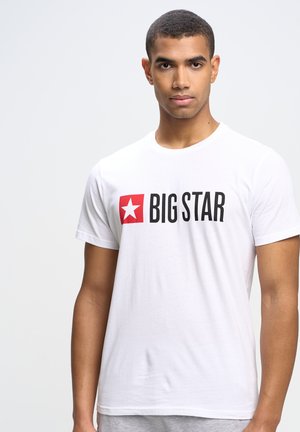 Hvid bomulds t-shirt med en rød firkant med en hvid stjerne og "BIG STAR" i fed sort tekst på forsiden. Korte ærmer, rund halsudskæring.