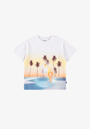 Fehér póló, amin egy gördeszkás mutat be egy trükköt egy kék gördeszkaparkban naplementekor, a háttérben pálmafákkal.