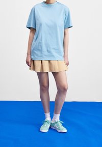 Jasnoniebieska bawełniana koszulka, beżowa plisowana spódnica, białe skarpetki z falbanką oraz miętowo-zielone trampki z białymi akcentami, na niebieskim tle.