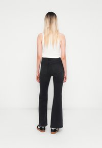 Black flared jeans with a high waist, featuring back pockets and a smooth texture. Paired with shiny black shoes and a white tank top.