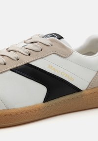 Biało-czarny skórzany sneaker z beżowymi zamszowymi akcentami, wyposażony w beżowe sznurowadła, teksturowaną gumową podeszwę oraz złote detale z logo.