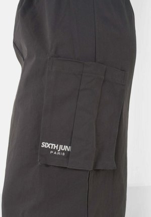 Pantalones cargo negros hechos de una tela de textura suave, con un bolsillo lateral y un logo de la marca bordado en blanco en el bolsillo.