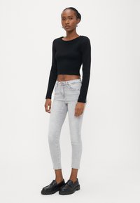 Μαύρο κοντό τοπ με μακριά μανίκια και στρογγυλή λαιμόκοψη, ανοιχτό γκρι τζιν στενής γραμμής και μαύρα chunky loafers. Ομαλή υφή, εφαρμοστό σχέδιο.