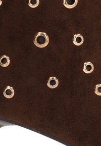 Material de gamuza marrón con ojales en tono dorado de varios tamaños, creando una apariencia texturizada con un diseño de superficie lisa y plana.
