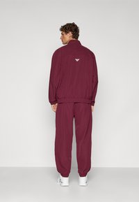 Trening de culoare băție, compus dintr-o jachetă cu fermoar și pantaloni asortați. Material moale, cu manșete elastice și detaliu de logo pe spate. Tenisi albi.